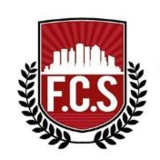 Logo of F.C.S featuring a red shield with a white city skyline and the initials "F.C.S" below it. The shield is flanked by black laurel branches on both sides.