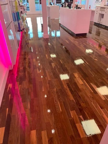 A retail store interior with shiny, polished wooden floors reflecting light. Displays with assorted beauty products are visible along the walls, and the lighting creates a warm, inviting atmosphere.